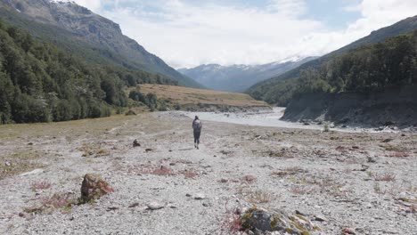 Joven-Caucásica-Caminando-Por-Un-Valle-Y-Un-Río-En-Un-Día-Soleado-Con-Una-Mochila-En-La-Pista-De-Dardos-Rees,-Nueva-Zelanda