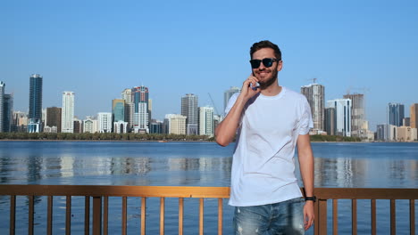 Happy-young-man-walking-on-the-street-and-looking-aside-while-talking-by-his-phone