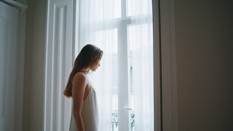 una chica sensual mirando la ventana del dormitorio de cerca. una mujer tierna relajándose por la mañana.