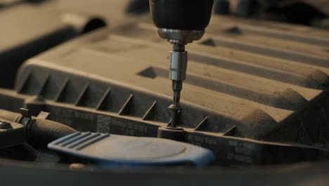 a screwdriver tightens a screw under the hood of a car