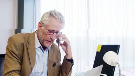 hombre de negocios hablando por teléfono móvil mientras trabaja en el escritorio