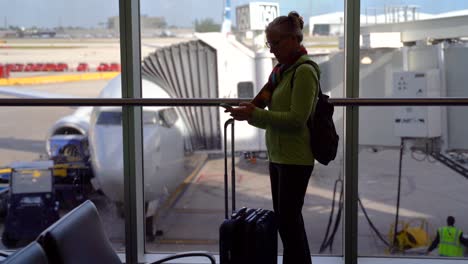 silueta de mujer viajera con equipaje revisando su celular frente al avión preparándose para abordar