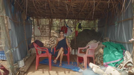 cinematic slow motion shot of an indian fashion model sitting in a plastic chair in a blue, red and orange sustainable fashion dress in goa india, slomo