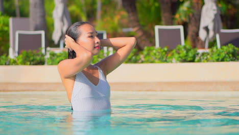 una joven asiática apasionada toca su cabello mojado dentro del agua de la piscina de un hotel exótico con los ojos cerrados al atardecer en el hotel de miami, toma de retrato