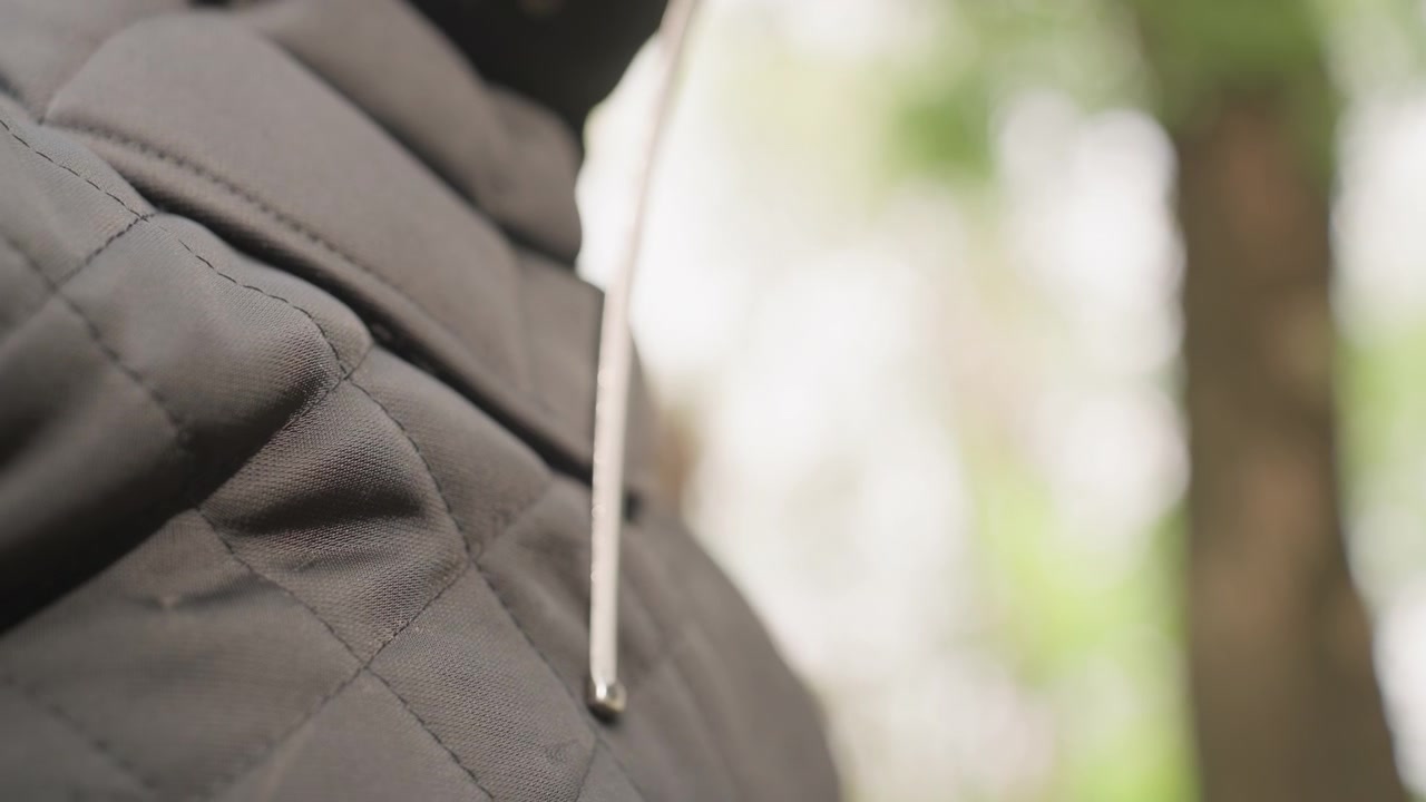 Close up of person wearing dark gray quilted fabric with visible stitching as ice pick is inserted into material. background shows blurred green foliage indicating outdoor setting