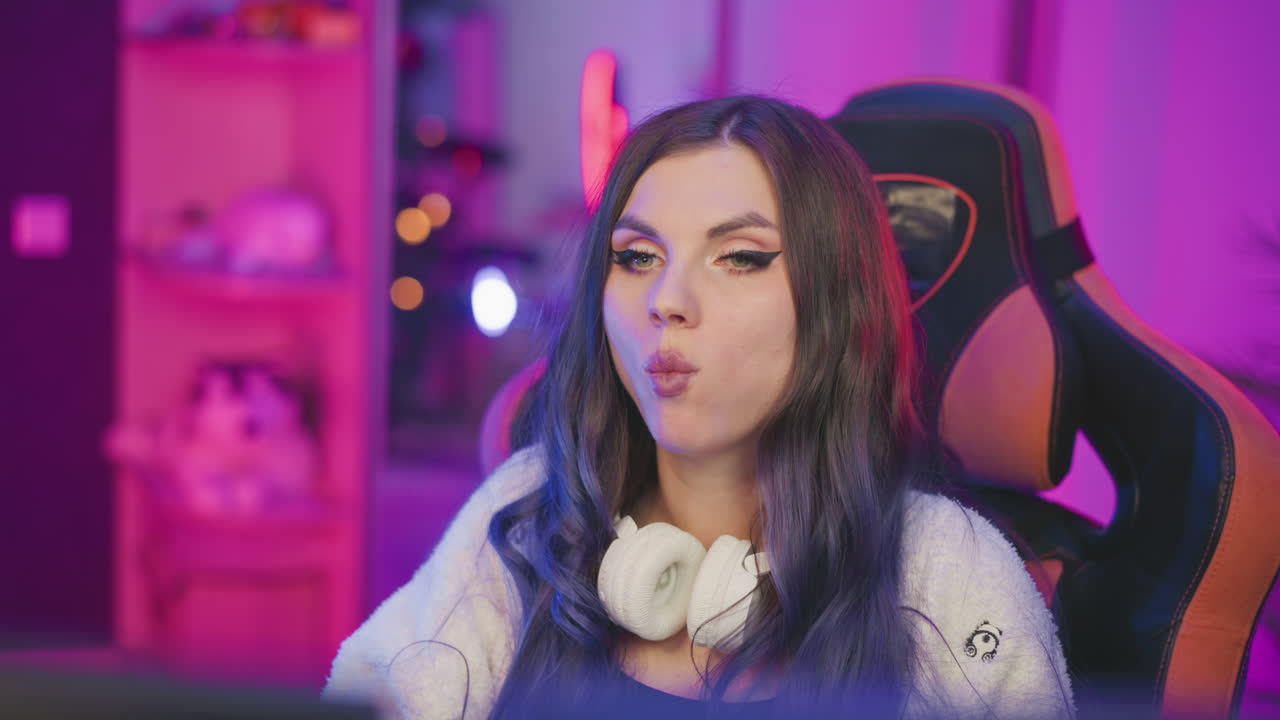 Girl with long hair eating popcorn in cozy setting while adjusting her hair, surrounded by glowing colorful lights in studio with relaxed expression and headphones resting around her neck