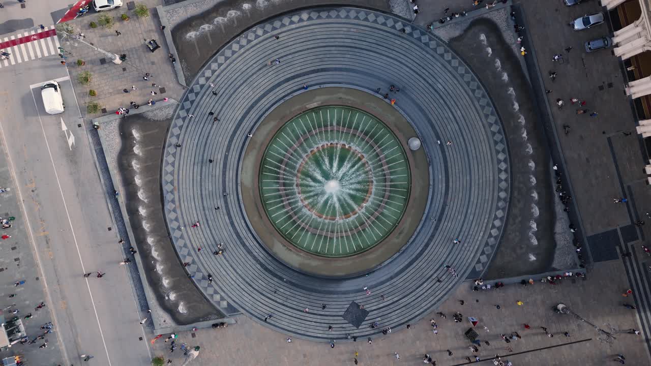 Genoa's ancient circular fountain, with people gathered around its steps and walkways, aerial view