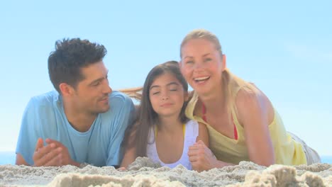 una pareja y su hija acostadas en una playa.