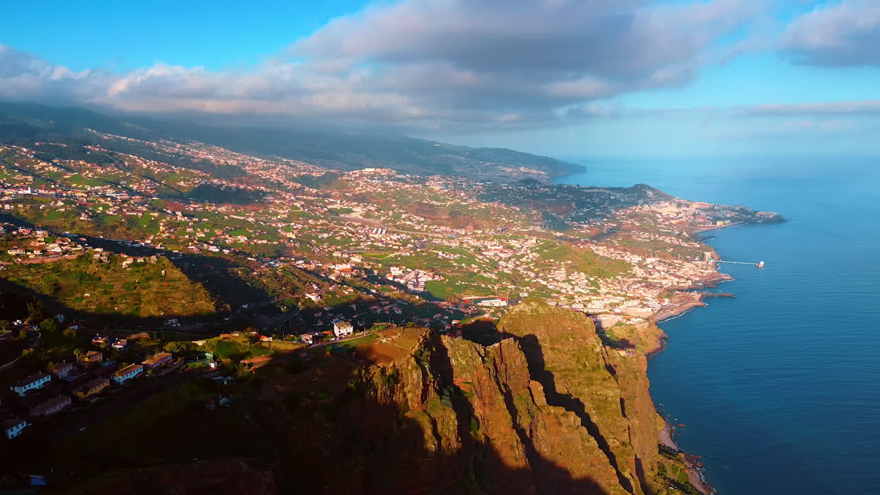 Footage high above the picturesque shore of the Madeira Islands, Portugal. Inhabited area on the slope of a rocky coast of the Atlantic Ocean. Dramatic cloudscape covering the backdrop.
