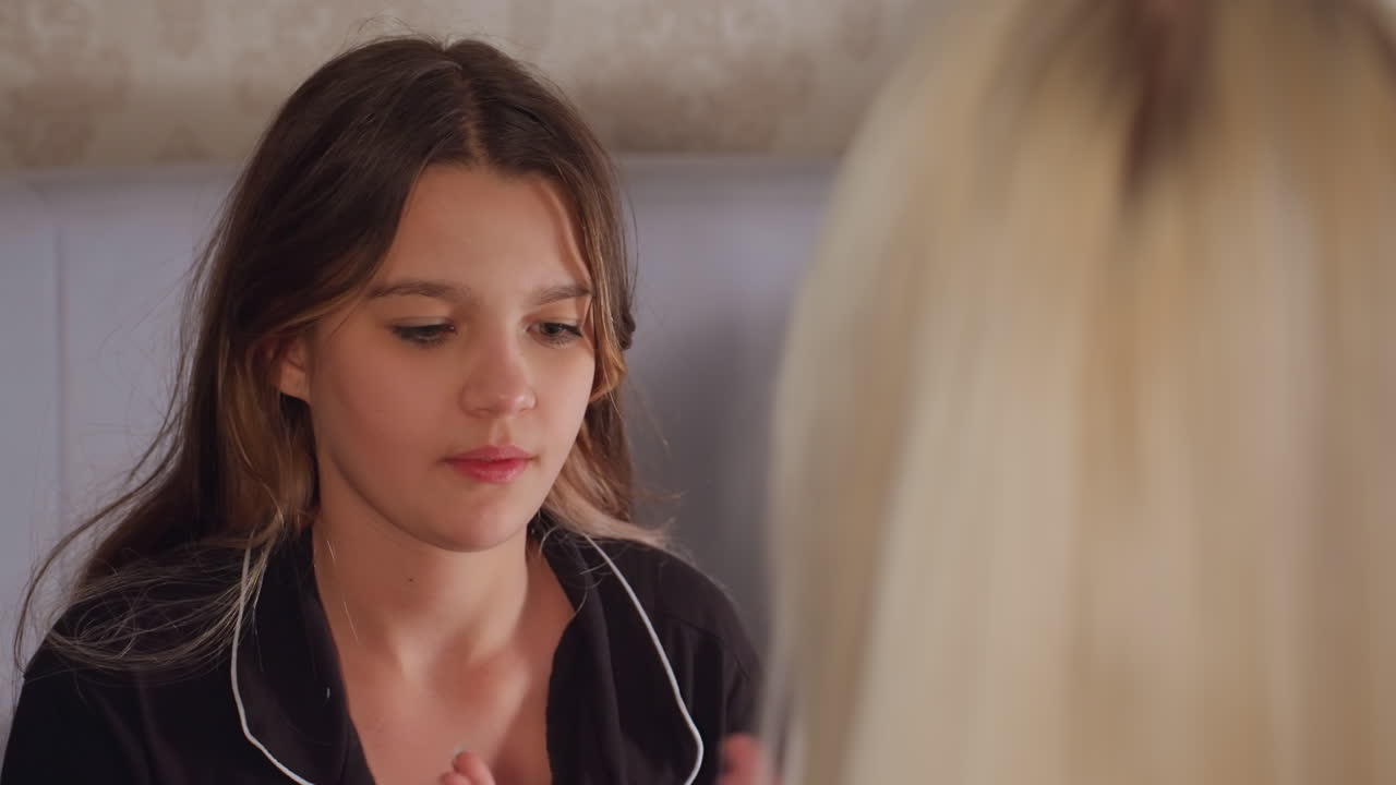 Close up of young girl in black pajamas clapping hands playfully with unseen partner, showing soft smile and joyful expression during relaxed indoor bonding