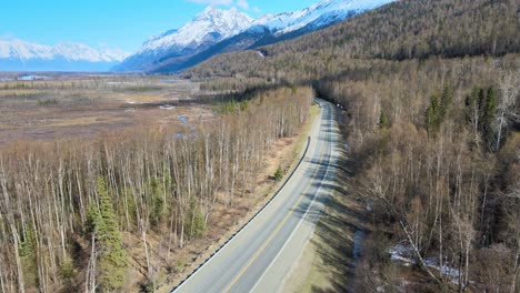 Vista-Aérea-De-La-Carretera-Rural-Con-Montañas-A-La-Derecha-Y-Pantano-A-La-Izquierda-En-La-Primavera-Antes-De-Que-El-Follaje-Se-Vuelva-Verde