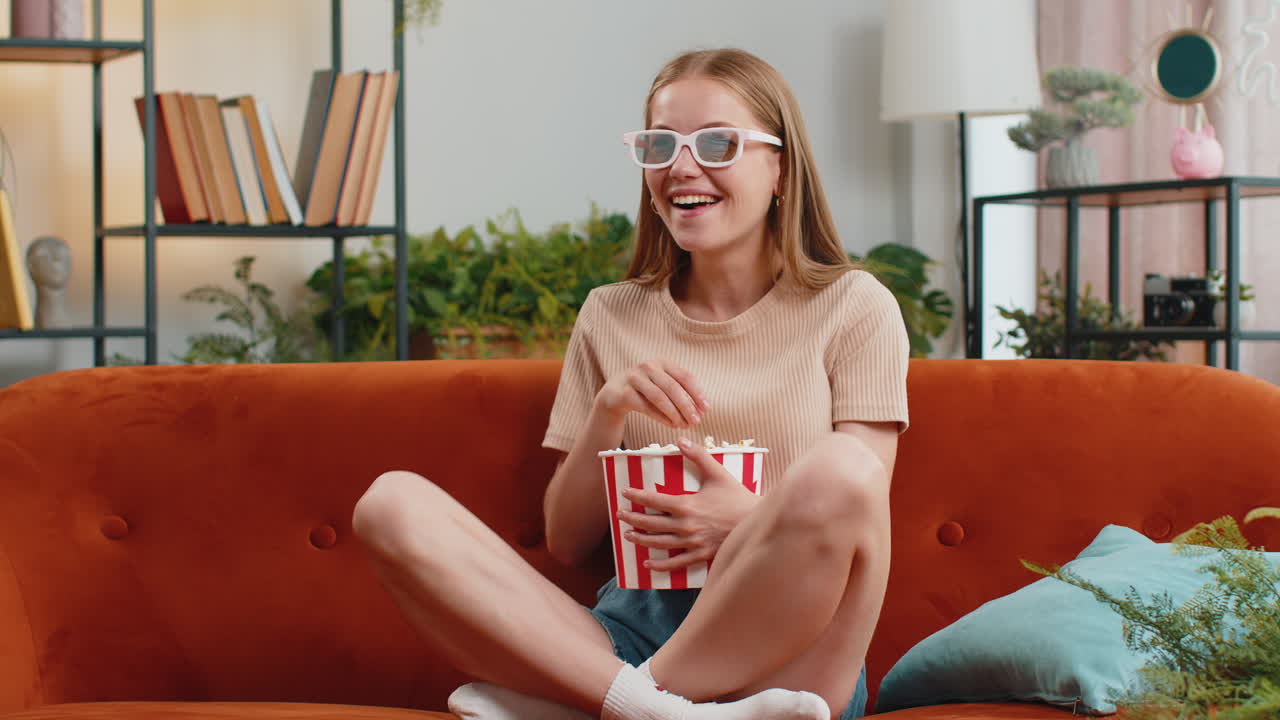mujer sentada en el sofá comiendo palomitas de maíz y viendo interesantes películas de televisión en 3d, juegos deportivos en línea en casa