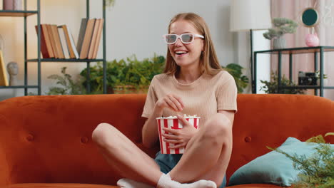 woman sitting on couch eating popcorn and watching interesting tv 3d film, sport game online at home