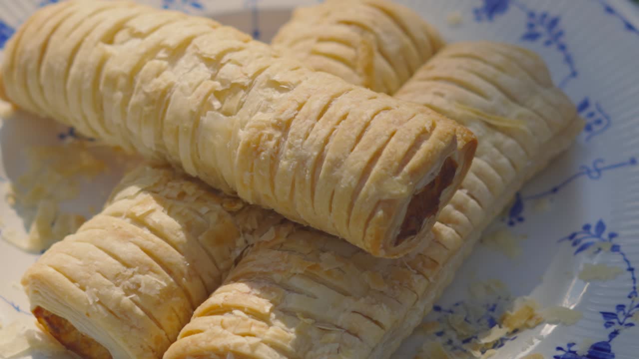 Slow Motion Baked Pork Sausage Roll Falling with Flakey Pieces of Pastry Flying Off. Delicious Fresh Bakery Product. Traditional British Pork Meat Wrapped in Puff Pastry.