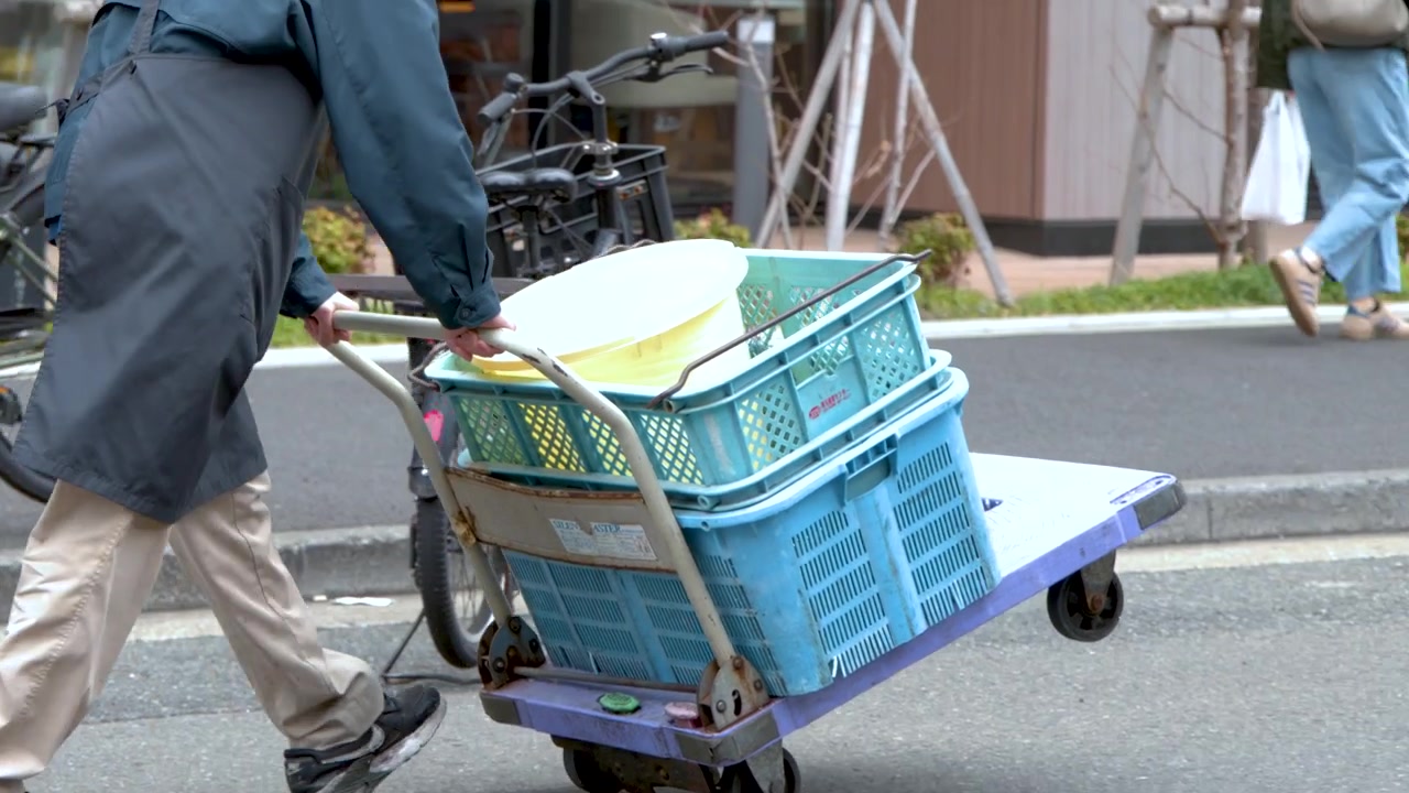 Un fattorino spinge un carrello a mano carico lungo una strada urbana a Tokyo, Giappone.