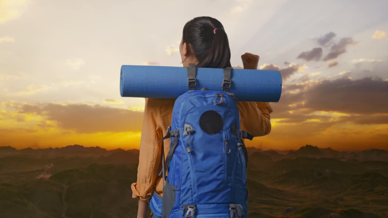 vista posterior de una excursionista femenina con una mochila de montañismo gritando el objetivo celebrando el éxito mientras estaba de pie en la cima de la montaña durante el atardecer