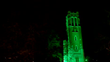 Beaumont-Tower-on-the-campus-of-Michigan-State-University-lit-up-at-night-in-green-in-honor-of-the-victims-of-the-February,-2023-mass-shooting-with-close-up-video-close-up-panning-left-to-right