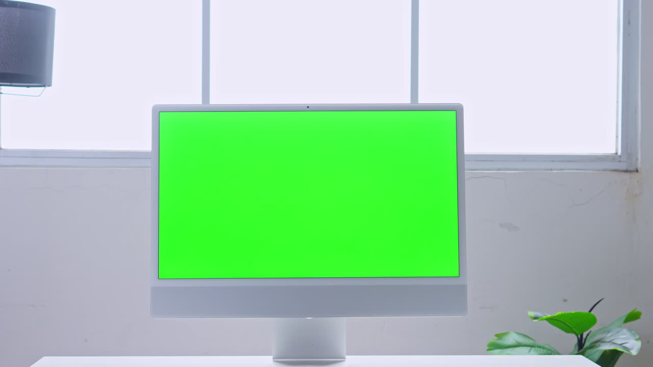 Professional office setup with green screen monitor on white desk against window