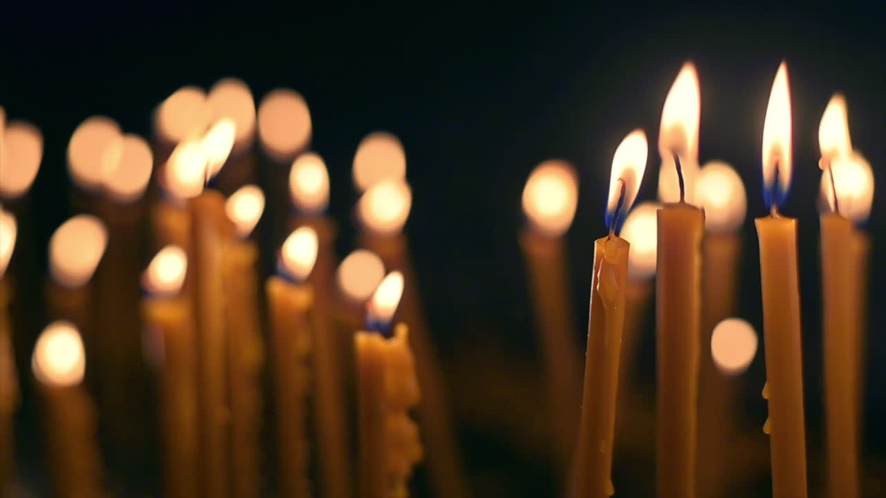 Close view of lots of burning candles with black background. Slow motion