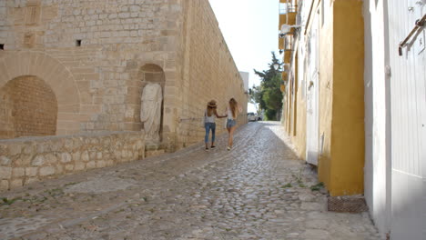 two female friends walking through old ibiza, back view