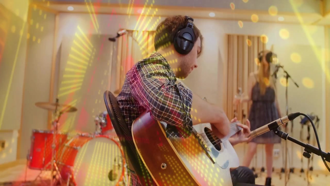 Chitarrista che accorda vicino al microfono, strimpellando mentre il vocalist canta per registrare, con una sovrapposizione di luce che sale sulla band