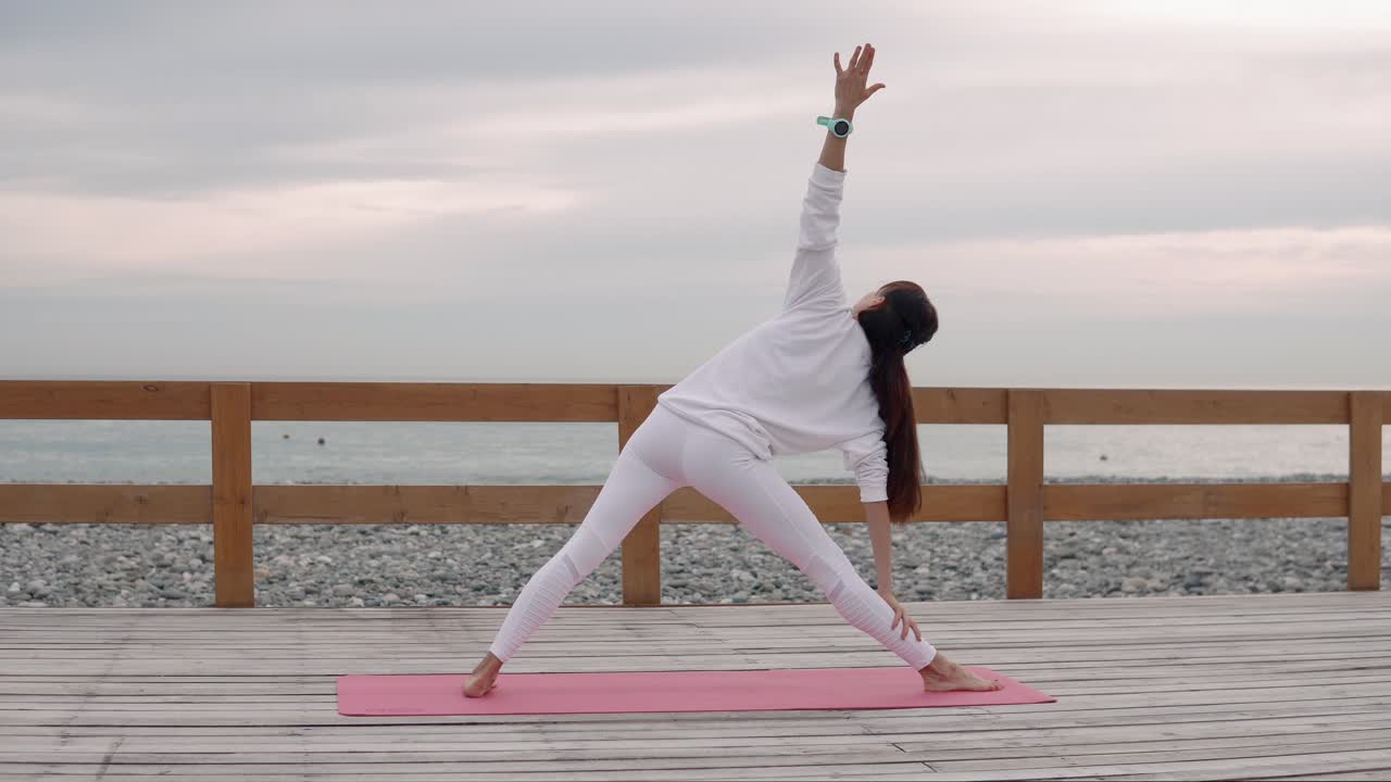 mujer practicando la postura del triángulo del yoga junto al mar