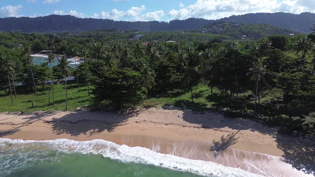Aerial drone footage of a hidden tropical beach in Koh Lanta, Thailand, featuring swaying palm trees, rugged rocky coastline, golden sand, and clear blue water, with no people