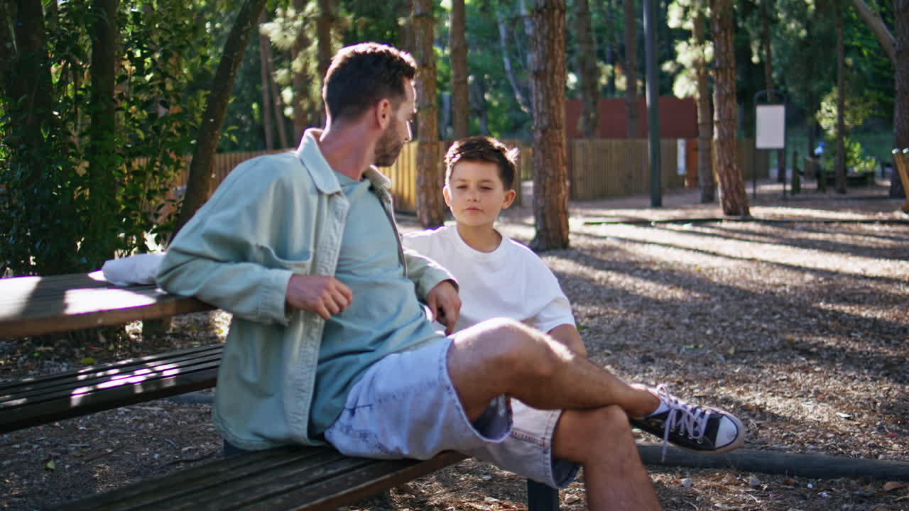 Father talking lovely son relaxed park weekend. Happy parent boy sitting bench