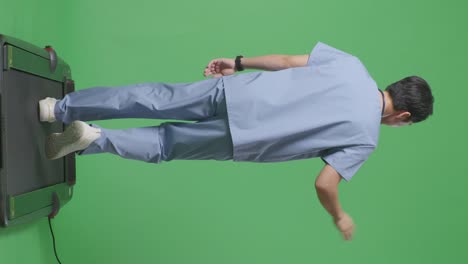 cuerpo lleno de vista trasera médico masculino asiático con estetoscopio agitando la mano y sonriendo mientras camina en el fondo de la pantalla verde en el hospital