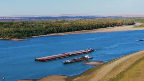 Aerial-shot-of-a-dredger-unloading-dredged-sand-on-a-big-river,-other-ships-passing-by,-sunny-day