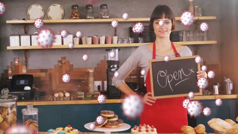 animation of macro covid-19 cells floating over happy caucasian female chef holding open sign