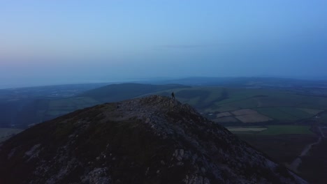 aerial - flying from front to behind the man standing on top of the mountain watching beautiful sunset-sunrise over the peaks