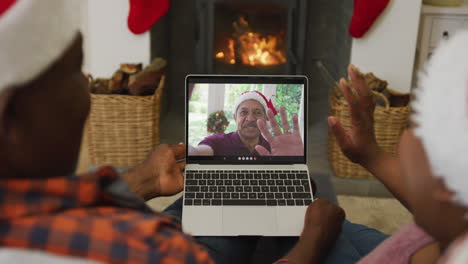 pareja afroamericana con sombreros de santa usando una computadora portátil para una videollamada de navidad con un hombre en la pantalla