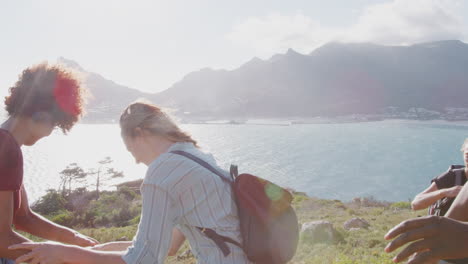 group of young friends hiking standing on cliffs by coast and looking at beautiful view