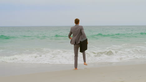 Rückansicht-Eines-Kaukasischen-Geschäftsmannes,-Der-Mit-Einer-Aktentasche-Am-Strand-Springt,-4k