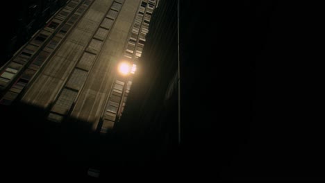 sunlight reflects off facade of tall, concrete residential building in shadowed urban area, stark contrast between light and darkness. architectural details enhance city modern, gritty aesthetic