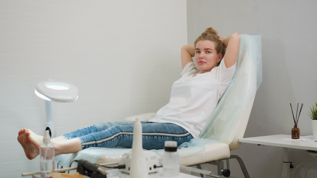 Woman sitting comfortably on salon chair with hands resting behind head, appearing calm and relaxed in brightly lit interior. Tools and decoration accentuate professional and peaceful atmosphere