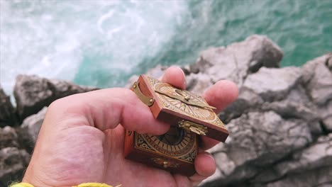 close up of human hand opening in slow motion a wooden engraved compass in a rocky coastal landscape