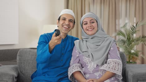 happy muslim couple laughing while watching tv