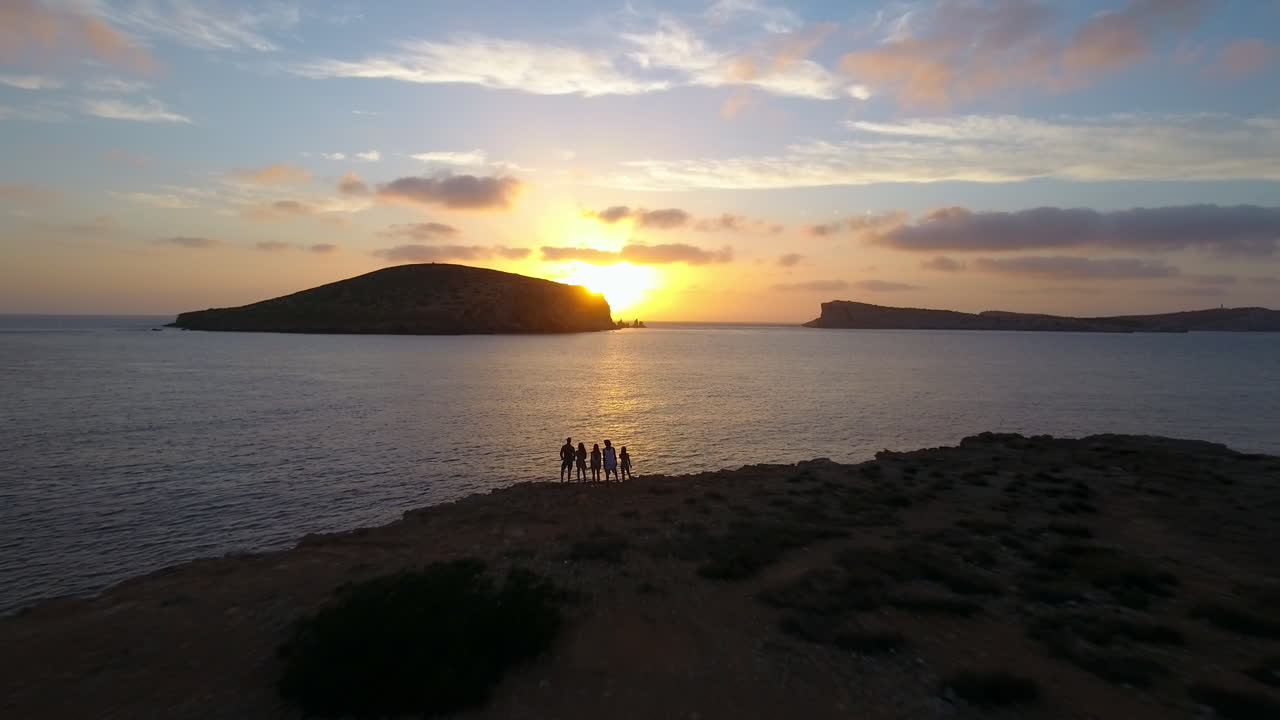 바다 위 에서 해 가 지는 것 을 지켜보는 절벽 에 있는 친구 들 의 공중 촬영