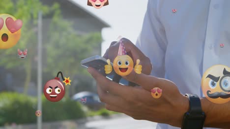 Animation-Von-Emoticons-über-Den-Händen-Eines-Gemischtrassigen-Mannes,-Der-Sein-Smartphone-In-Der-Stadt-Nutzt