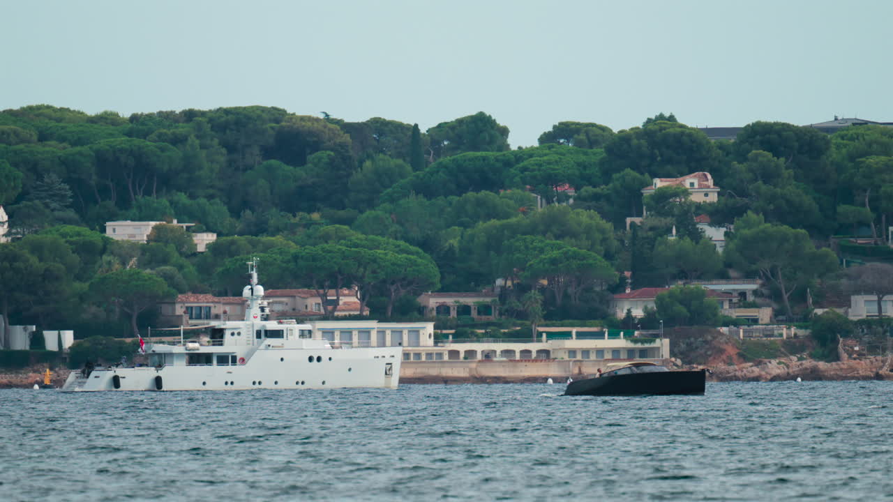 Elegant white yacht anchored off a scenic coastline surrounded by Mediterranean villas and lush pine trees