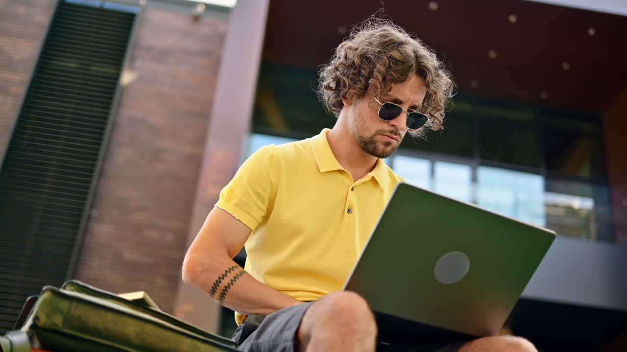 Man in yellow shirt talking standing on a bench and working on a laptop