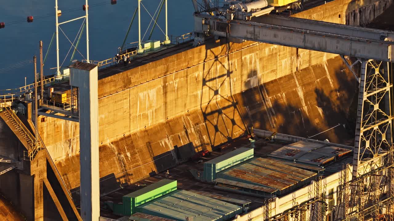 Industrial spillway dam wall and workers above Carpenter Dam hydroelectric facility in warm golden light, Arkansas
