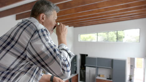 hombre bi-racial senior feliz bebiendo café en el piso de arriba aterrizando en casa, espacio de copia, cámara lenta