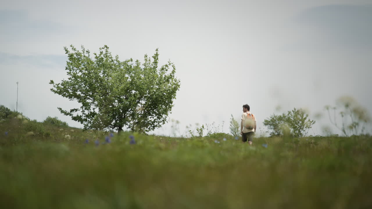 보라색 꽃이 만발한 산 슬라브니크의 푸른 초원 사이의 길을 걷고 있는 주황색 배낭을 든 등산객