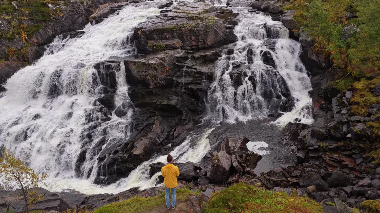 Riprese con drone di un uomo vicino a una cascata tra scogliere autunnali in Norvegia.
