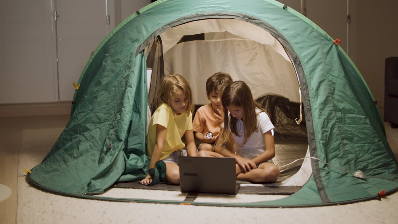 어린이 들 이 텐트 에서 노트북 에서 영화 를 보고 있다