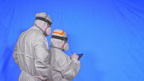 scientist virologist in respirator makes write in an tablet computer with stylus. man and woman wearing protective medical mask. chroma key blue.