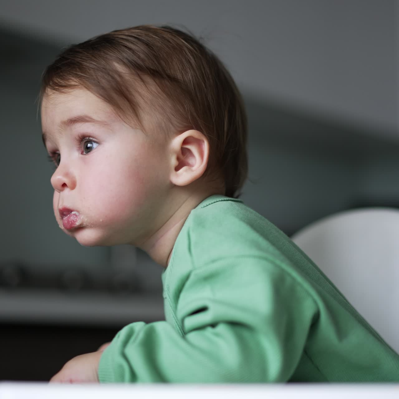 Una bambina adorabile dai capelli scuri viene nutrita dalla madre amorevole. La bambina curiosa si sporge in avanti sul seggiolone per guardare avanti. Sfondo sfocato